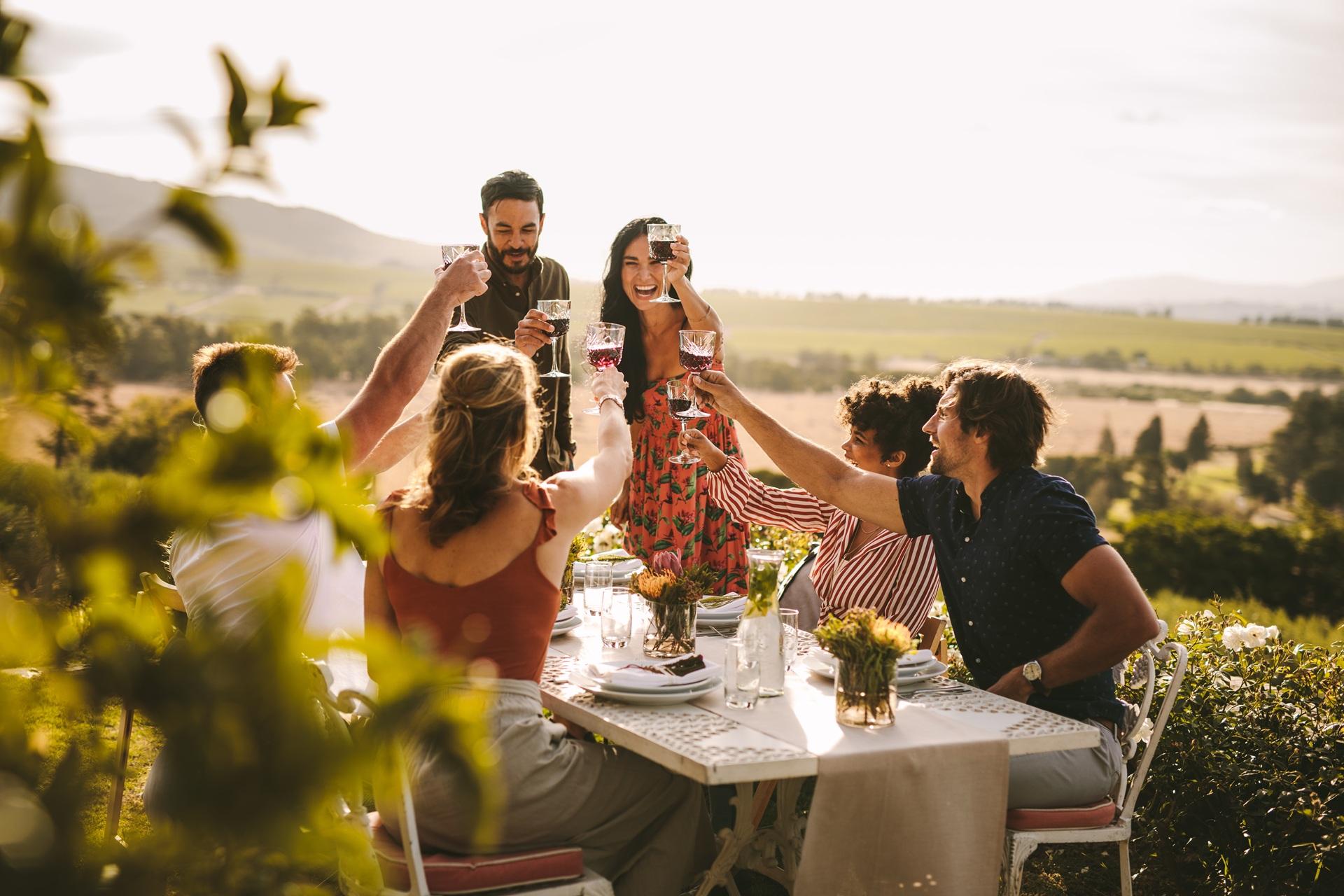Freunde stoßen beim Abendessen im Garten mit Wein an | Stehtisch